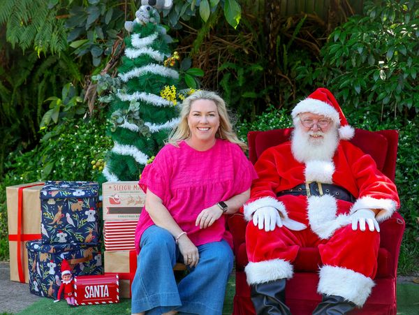 A woman sits next to a man dressed as Santa Claus with Christmas decorations around them.