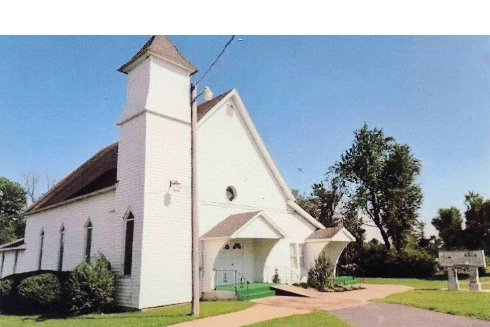 Outside picture of a white, wooden, one-story church.