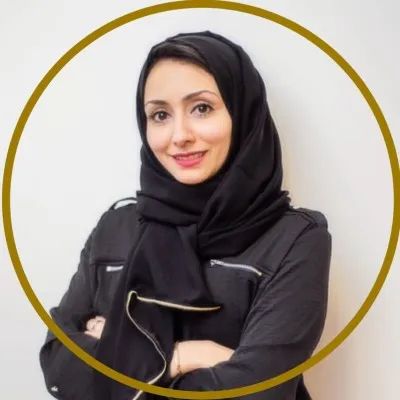 A smiling woman wearing a black hijab and outfit with arms crossed.