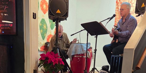 Two elderly men playing music indoors with instruments and microphones.