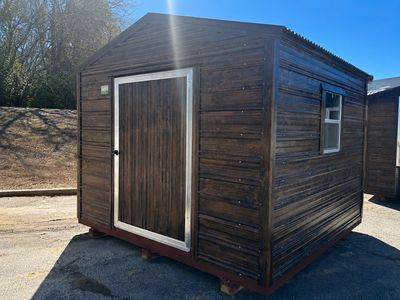 A dark brown wooden shed with a single door and window under bright sunlight.
