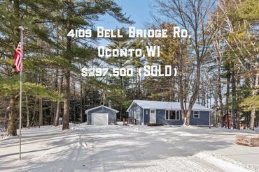 Blue house with detached garage in snowy wooded area, American flag flying.