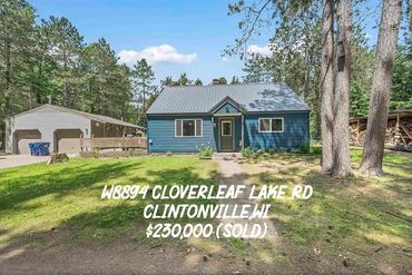 Blue house with detached garage on a spacious green lawn in a wooded area.