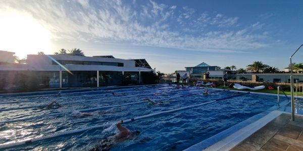 Swimmers practicing in an outdoor pool under a bright sky.
