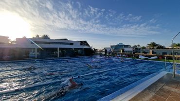 Swimmers practicing in an outdoor pool under a bright sky.