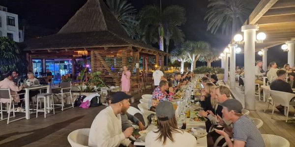 People dining outdoors at night in a lively restaurant with tropical decor.