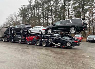 Car carrier trailer loaded with multiple vehicles in a parking lot.