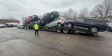 A truck transports multiple SUVs on a car carrier under a cloudy sky.