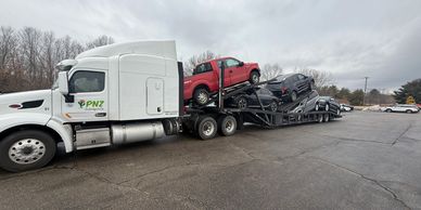 White truck carrying multiple cars on a car carrier trailer on a cloudy day.