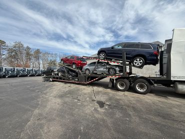 A car carrier truck loaded with damaged vehicles in a parking lot.