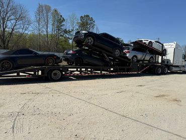 A car hauler truck carrying six cars on a sunny day.