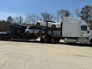 White truck transporting several cars on a sunny day.