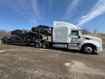 White semi-truck carrying multiple cars on a car carrier trailer.