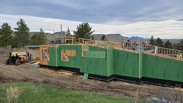A house under construction with green exterior sheathing and wooden framing.