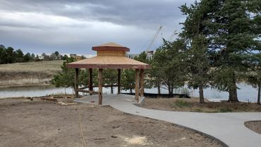 A wooden gazebo under construction near a pond with a cloudy sky.