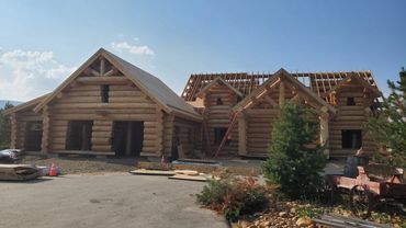 Log cabin under construction with wooden logs and roof framing.