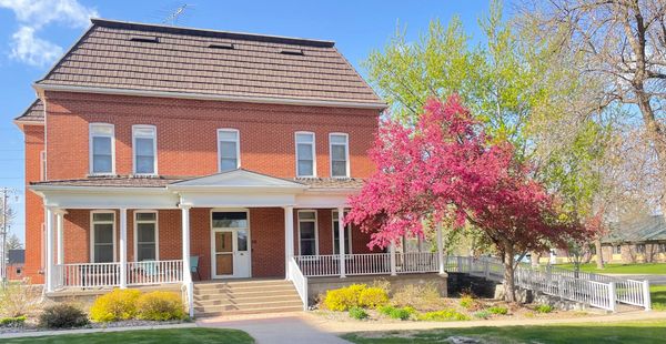 Large brick house with a pink flowering tree in front under a sunny blue sky.