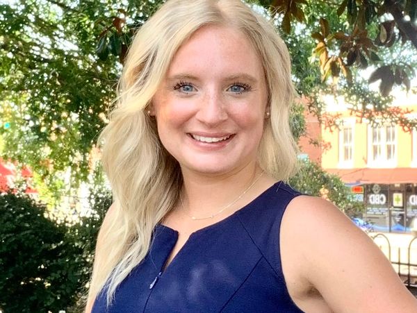Smiling woman with blonde hair in a navy blue dress outdoors.