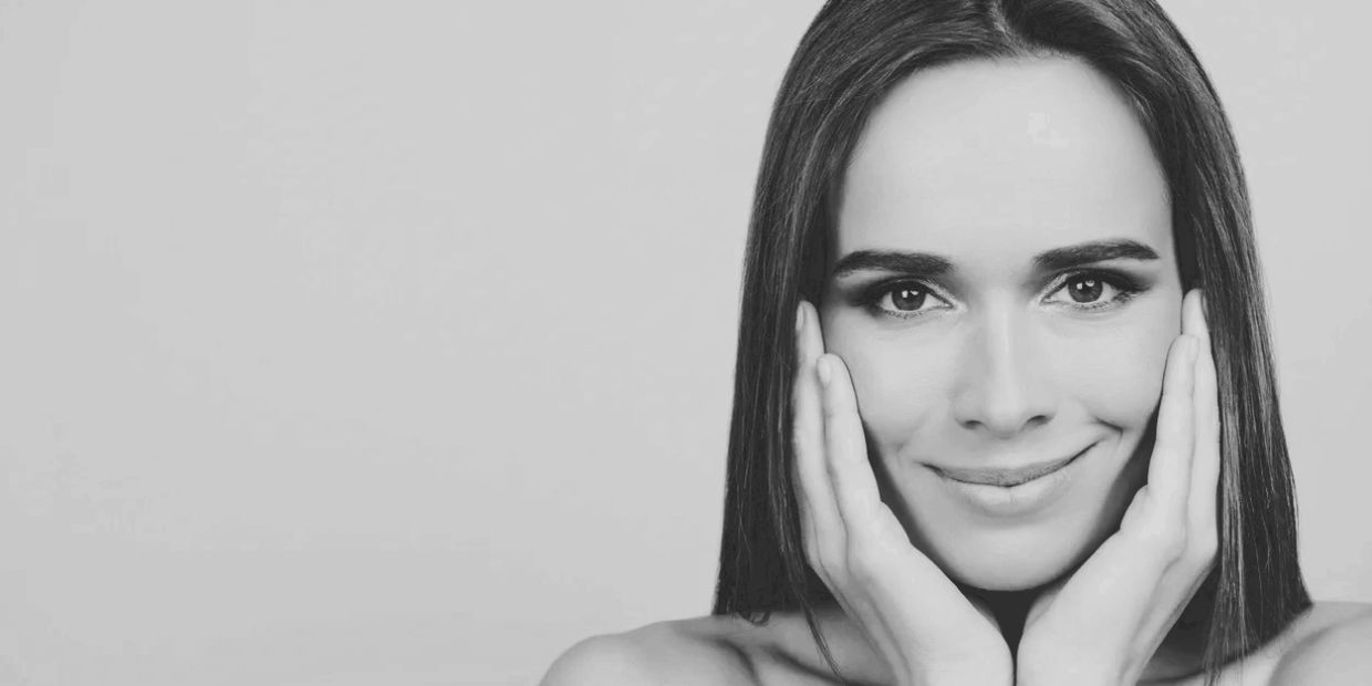 Black and white portrait of a smiling woman with hands on her face.