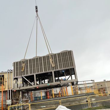 Large industrial equipment is being lifted by a crane at a factory site.
