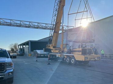 Yellow crane lifting equipment near industrial building on a sunny day.