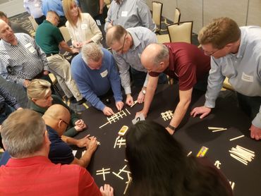 Group of people collaborating on a popsicle stick puzzle at a team-building event.