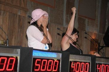 Two women reacting to scores on a game show scoreboard.