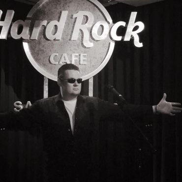 Man in sunglasses posing with arms outstretched on Hard Rock Cafe stage.