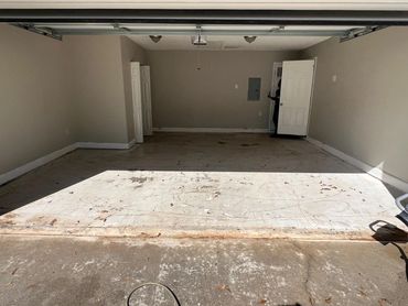 Empty garage with a concrete floor and two open doors at the back.