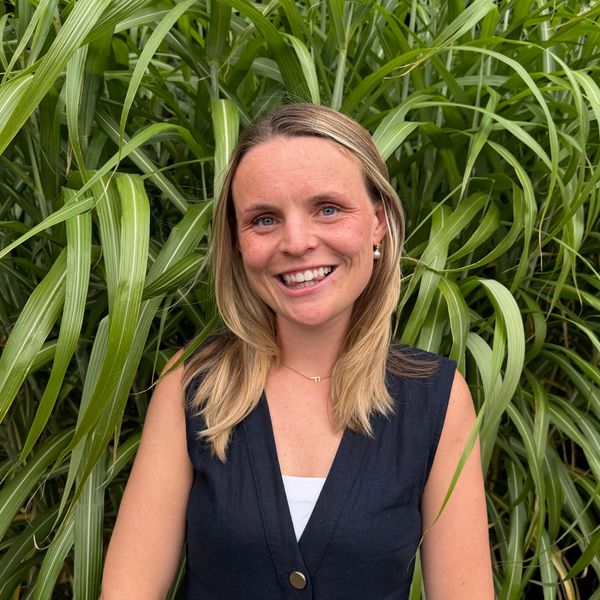 Smiling woman with blonde hair in front of green plants.