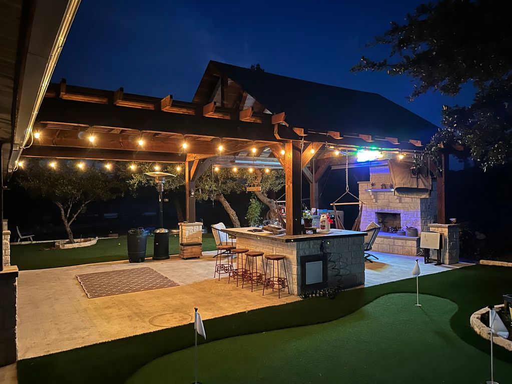 Cozy outdoor patio with bar, fireplace, and mini golf putting green at night.