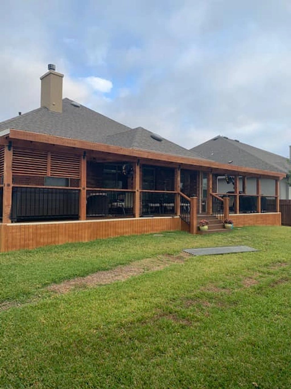 Spacious wooden porch attached to a house with a green lawn.