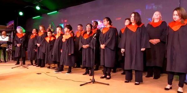 Choir singing on stage in black robes with orange collars.