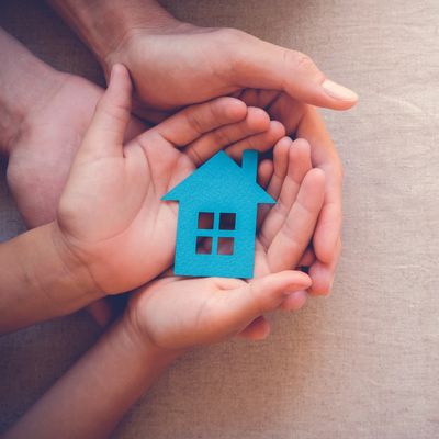 Hands holding a blue paper house together.