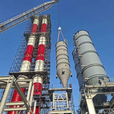 Industrial facility with large cylindrical structures and a crane lifting a component.