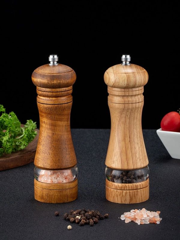 Wooden salt and pepper grinders with visible spices inside, set on a black surface.