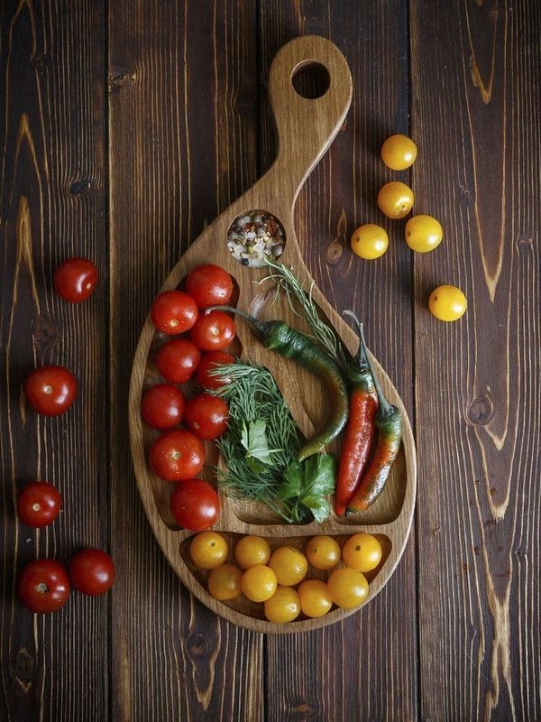 Fresh tomatoes, chili peppers, herbs, and spices on a wooden serving board.