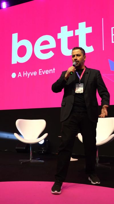 Homem falando no evento Bett em palco com fundo rosa.