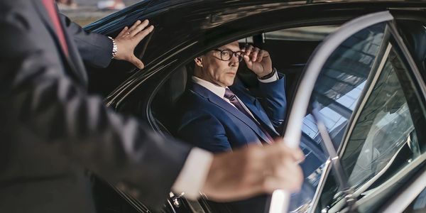a business man touching his glasses while inside of a luxurious vehicle