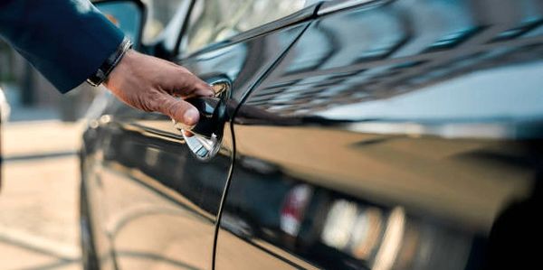Cropped photo of a male hand opening the door of a black car while standing outdoors.