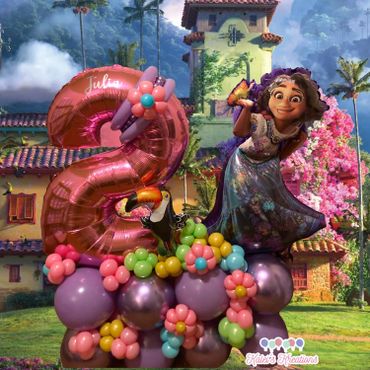Encanto's Mirabel standing on a bed of purple balloons with a toucan and large pink number balloon.