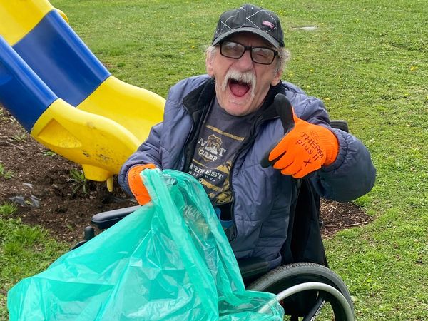 Supe happy man in a wheelchair with a bag of garbage during a cleanup