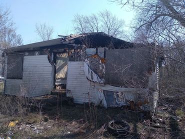Abandoned, dilapidated mobile home with extensive damage and overgrown vegetation.