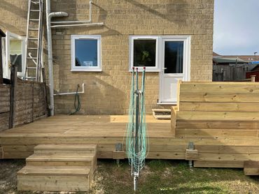 A newly built wooden deck with stairs outside a brick house under daylight.