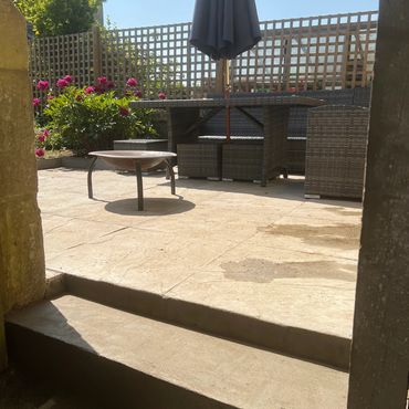 Sunny patio with wicker furniture, a closed umbrella, and a fire pit.