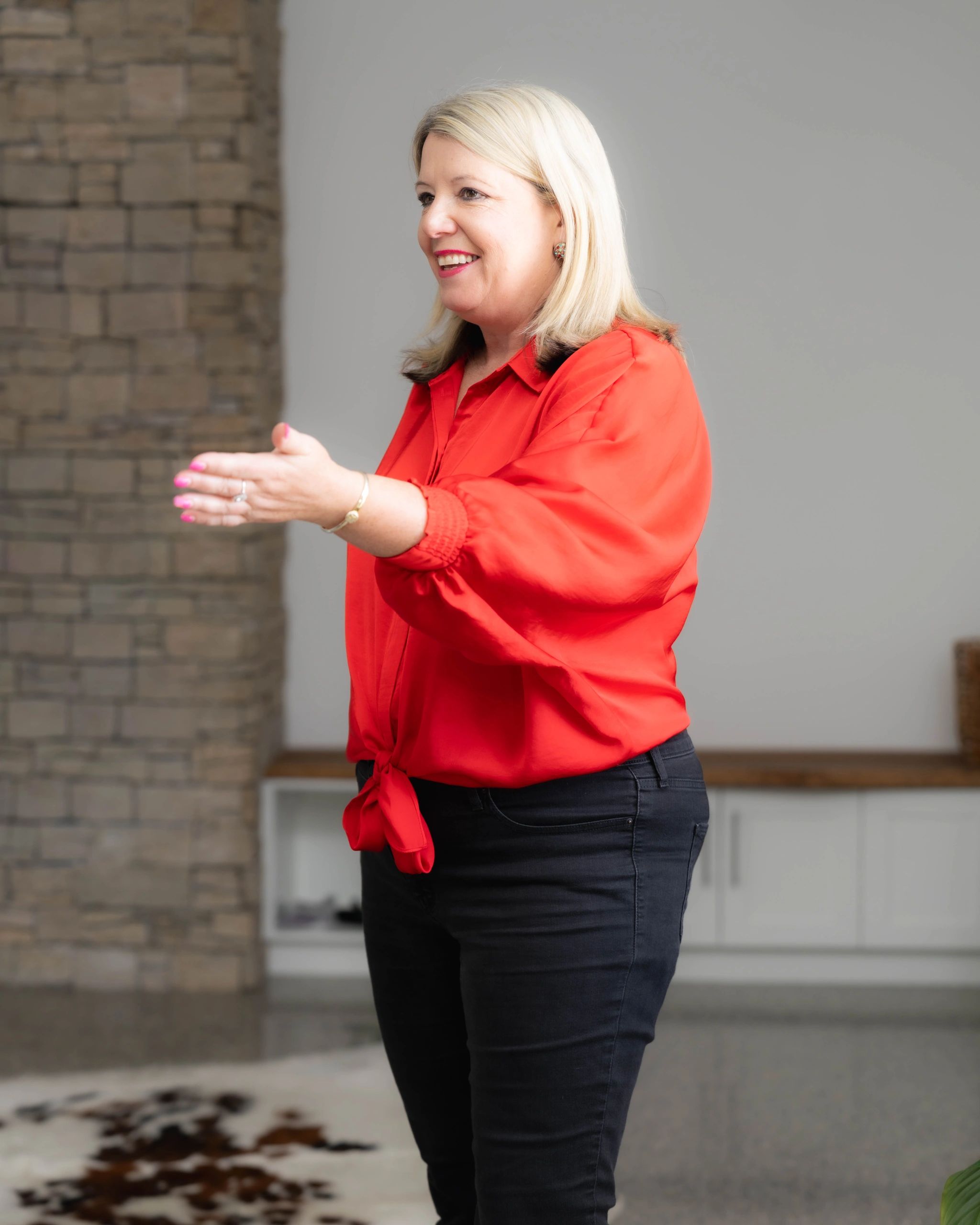 Woman smiling and gesturing with her hand indoors.