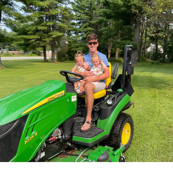 Man sitting on a John Deere tractor holding two young children.