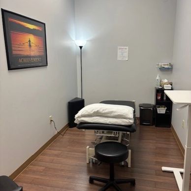 A clean, organized medical examination room with a treatment table and stool.