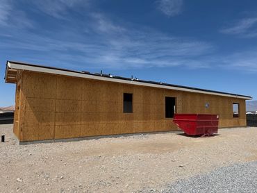 Wood-framed house under construction with a red dumpster outside.
