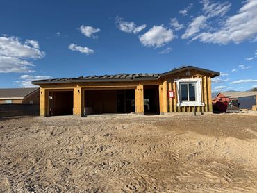 A wooden house under construction with a large front yard of dirt.